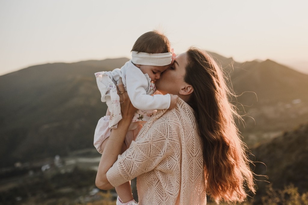 Mother gently kissing her baby at sunset, a peaceful moment of presence and connection